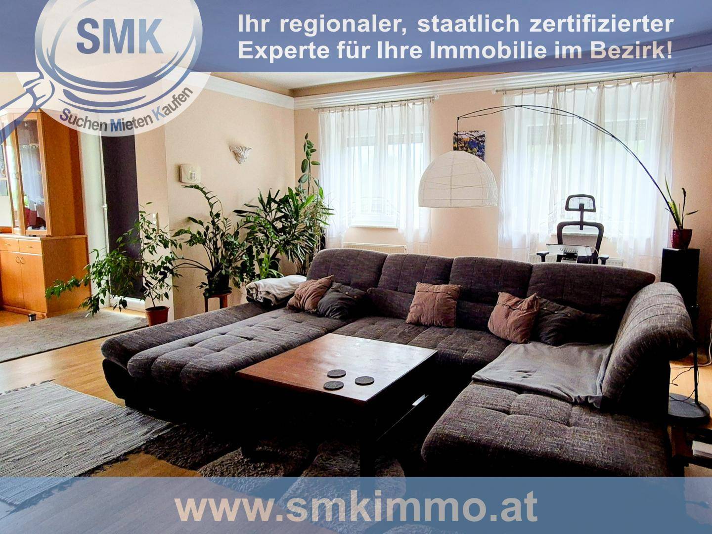 Gemütliches Wohnzimmer mit großem Ecksofa, vielen Pflanzen und Vorhängen an den Fenstern.
