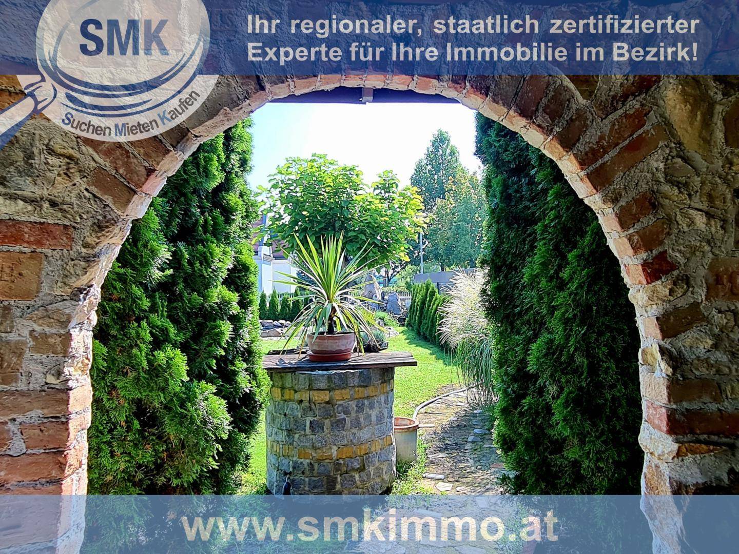 Blick durch einen Steinbogen in einen gepflegten Garten mit Bäumen und Pflanzen.