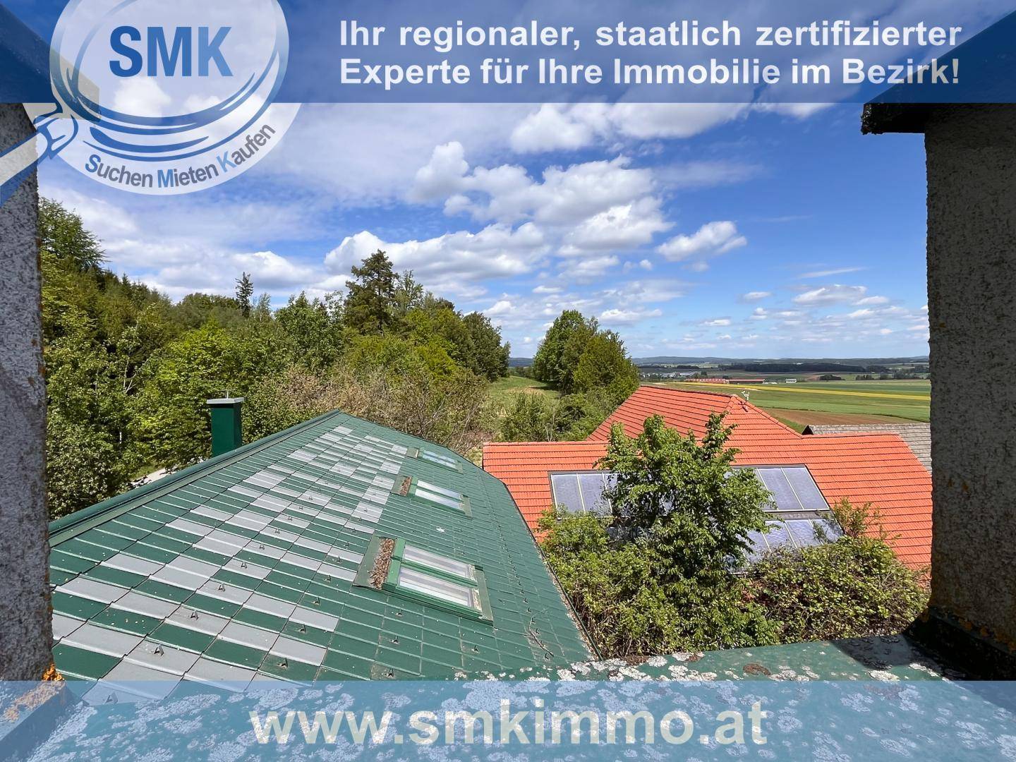 Panoramablick über Dächer und die umliegende grüne Landschaft unter blauem Himmel.