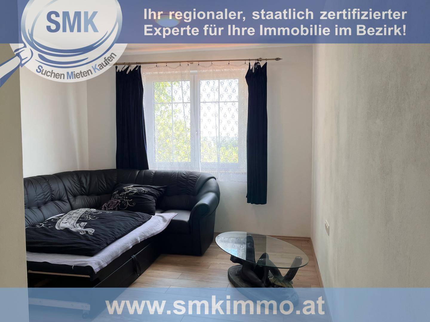 Gemütliches Zimmer mit schwarzem Ledersofa, Couchtisch und Fenster mit Vorhängen.