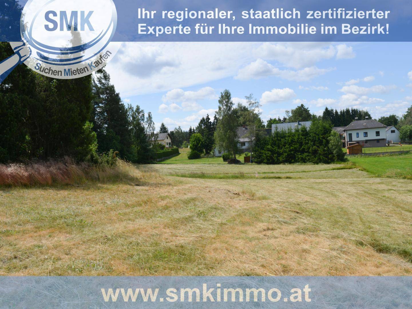 Ländliche Landschaft mit einem weiten Feld, Bäumen und Häusern in der Ferne unter blauem Himmel.