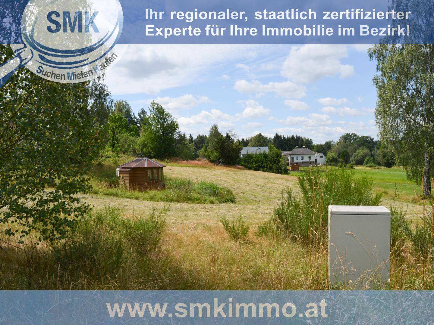 Weitläufiges Feld mit einem kleinen Holzpavillon und Häusern im Hintergrund unter blauem Himmel.