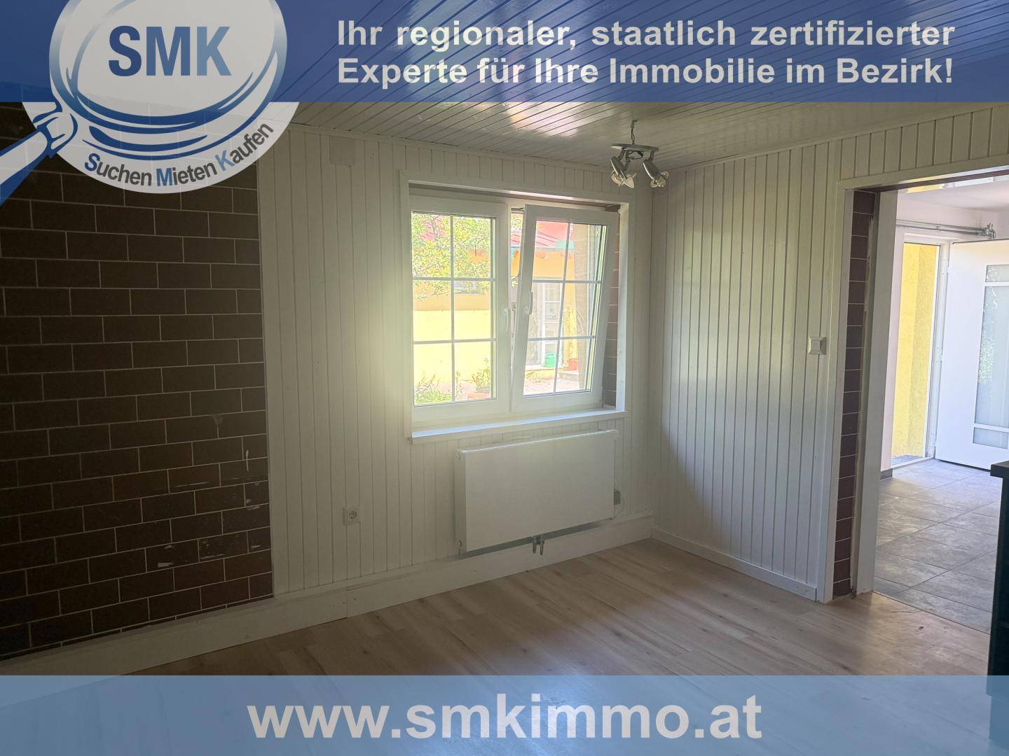 Raum mit Holzwänden und einer Ziegelwand, einem Fenster und Heizkörper, bietet rustikalen Charme.