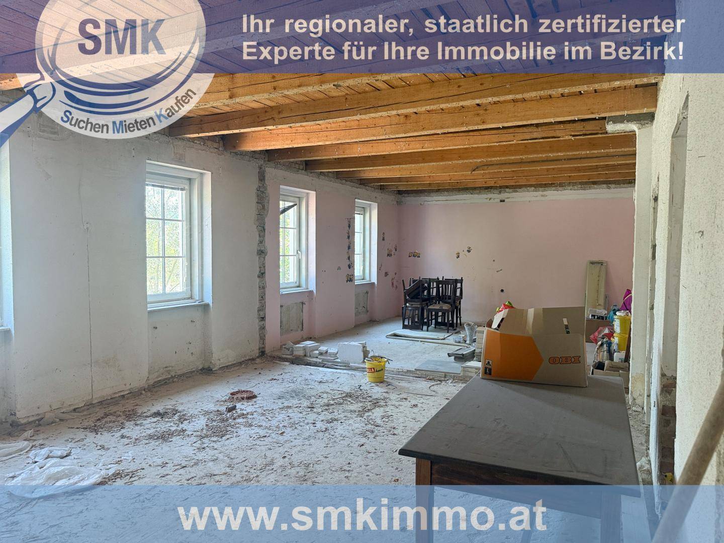Innenraum im Rohbauzustand mit freiliegenden Holzbalken, rosa Wänden und Betonboden.