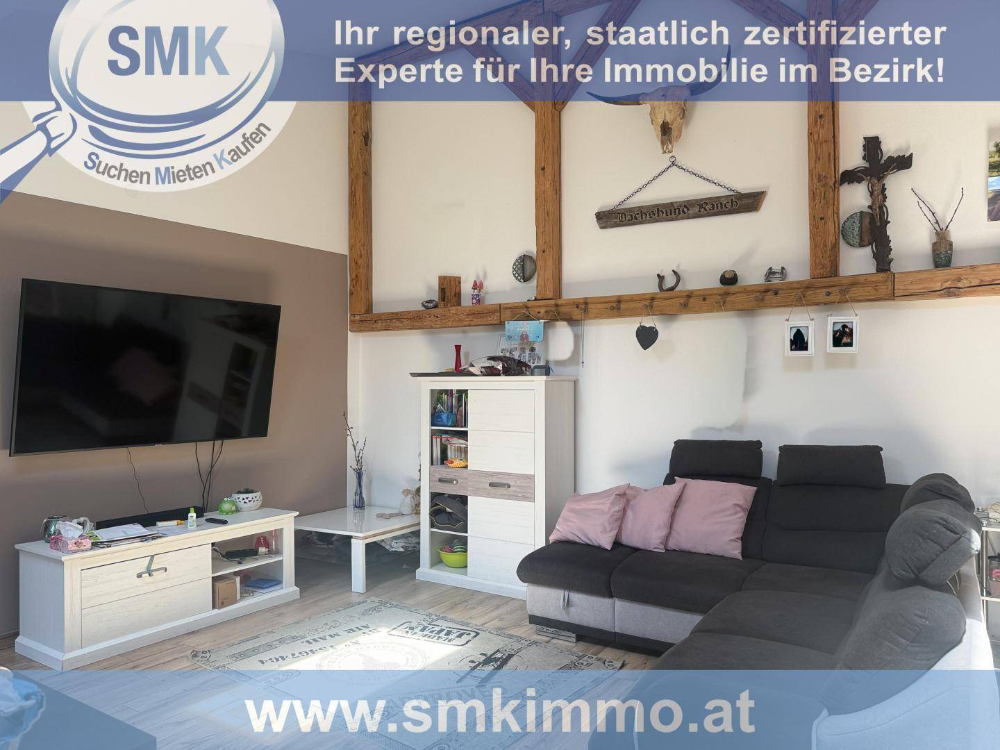 Gemütliches Wohnzimmer mit bequemer Couch, Fernseher und rustikalen Holzbalken an der Decke.