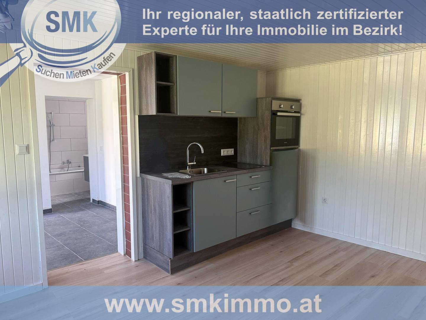 Kleine Küchenzeile mit modernen grauen Schränken und integriertem Backofen in einem Raum mit Holzverkleidung.
