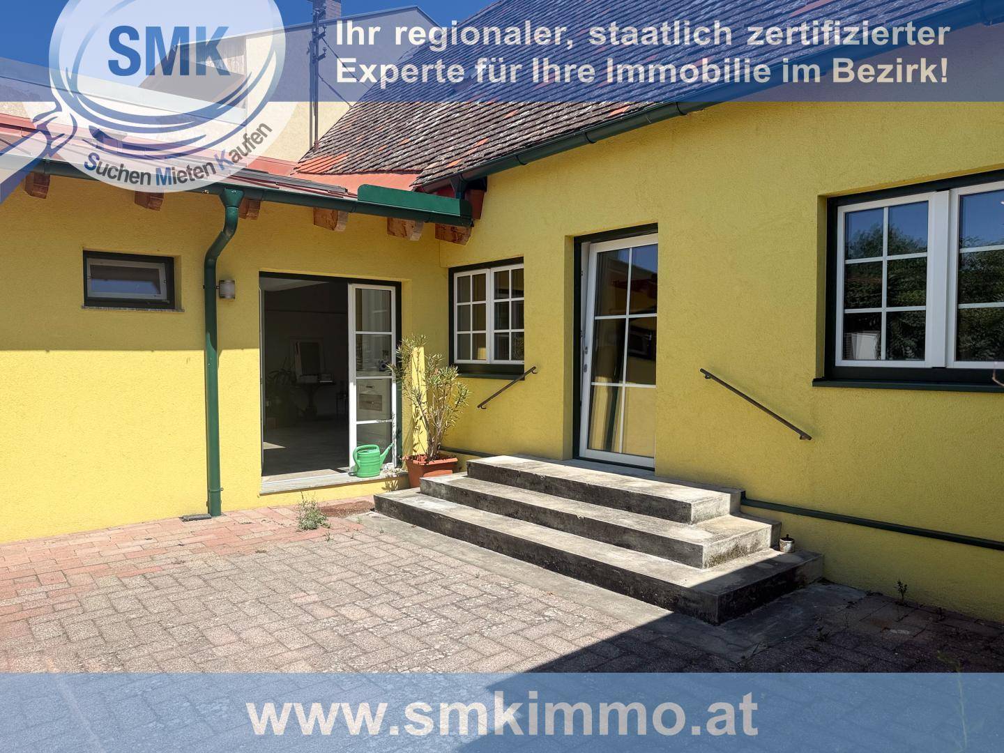 Gelbes Haus mit gepflasterter Terrasse und Stufen, umgeben von einem kleinen Gartenbereich.