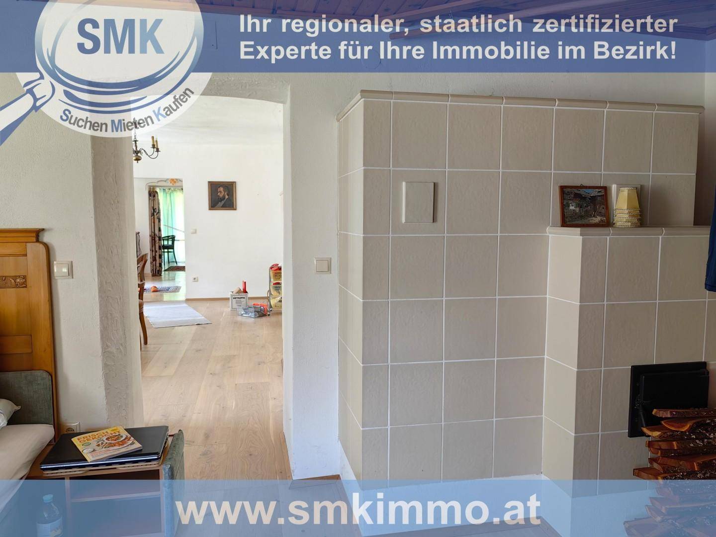 Wohnbereich mit traditionellem Kachelofen und Holzboden, der in einen weiteren Raum führt.