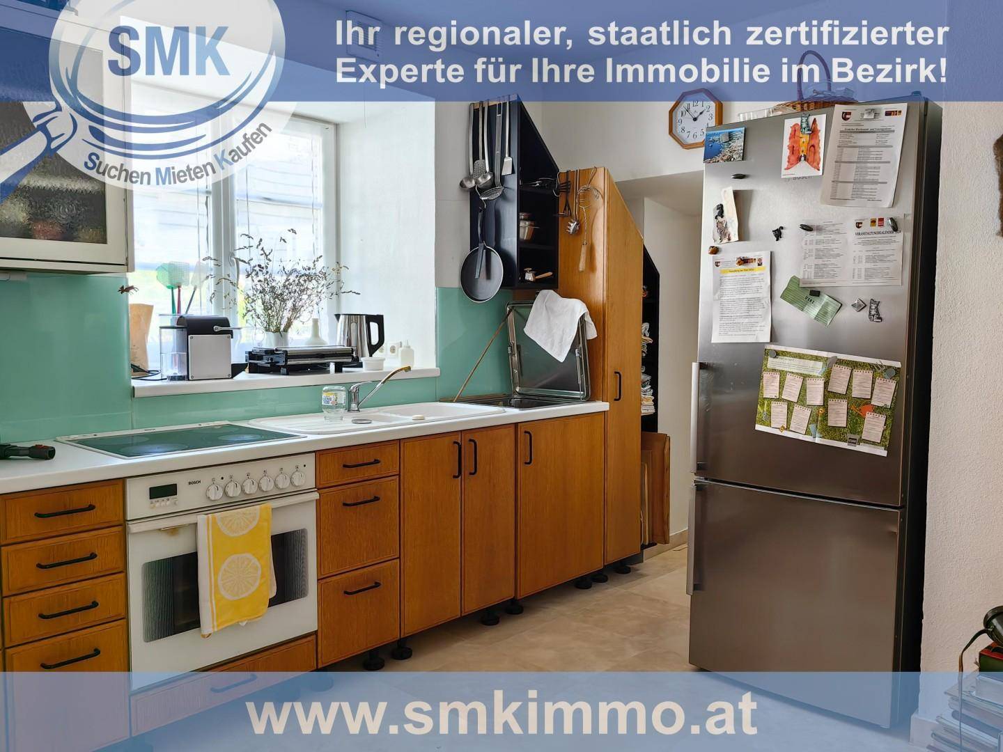 Funktionale Küche mit Holzschränken, Elektroherd und Kühlschrank, hell durch ein Fenster.