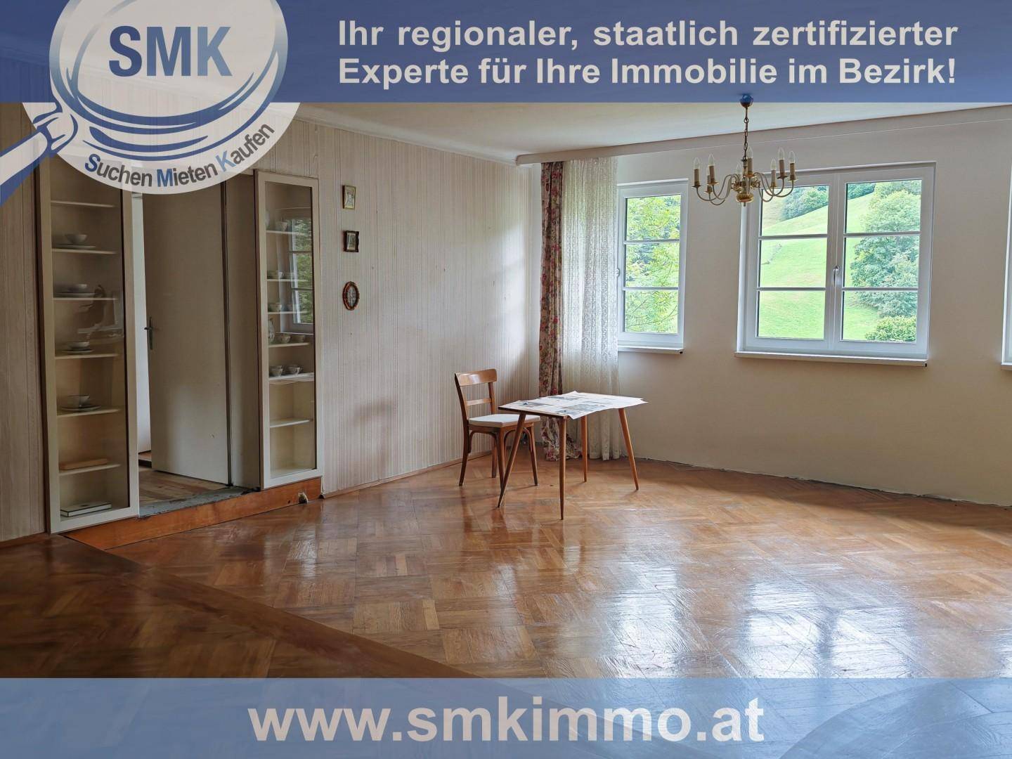 Großes Wohnzimmer mit Parkettboden, Kronleuchter und zwei Fenstern mit Blick ins Grüne.