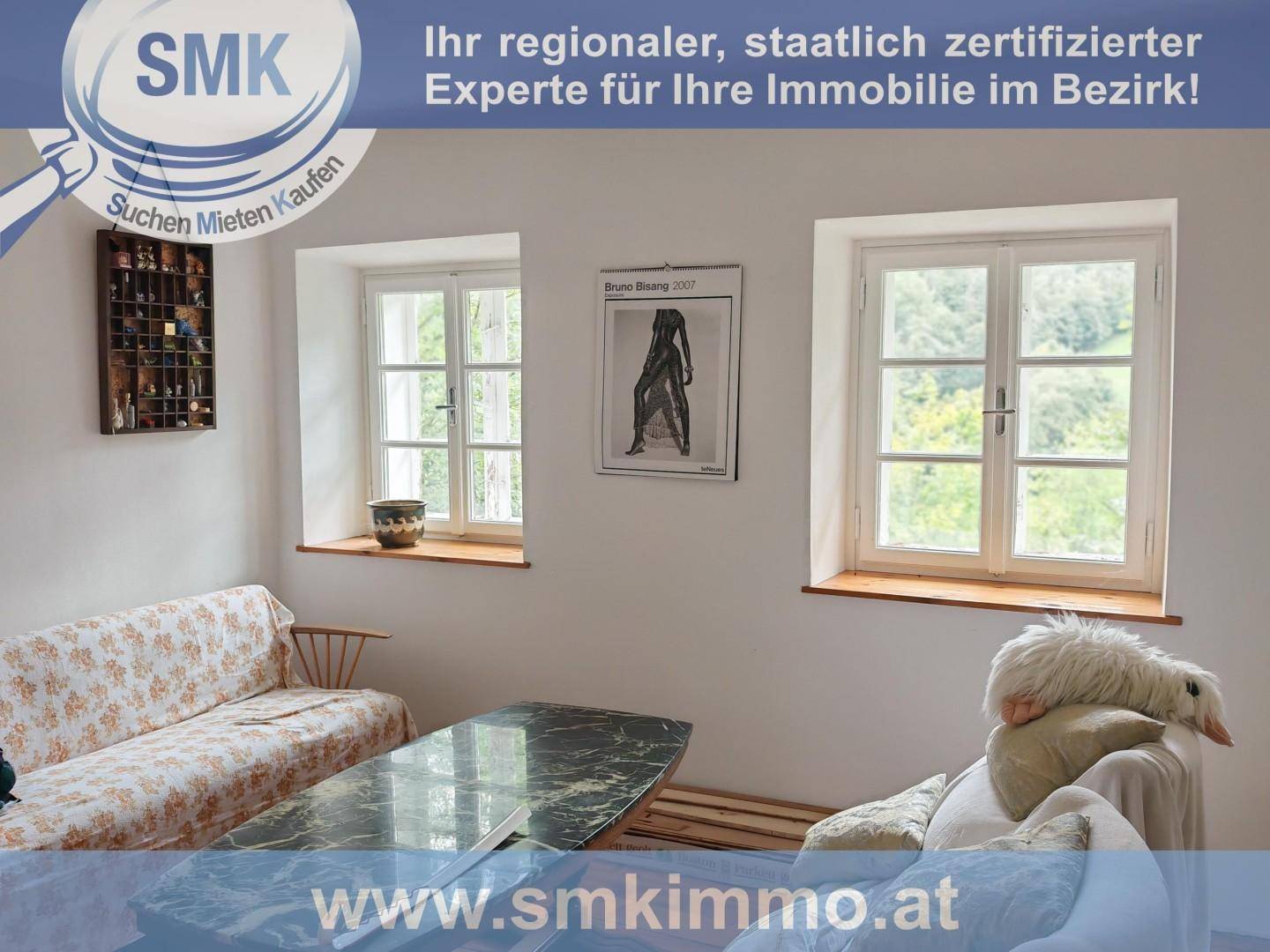 Helles Wohnzimmer mit Sofa, Couchtisch und zwei Fenstern, die den Blick ins Grüne freigeben.