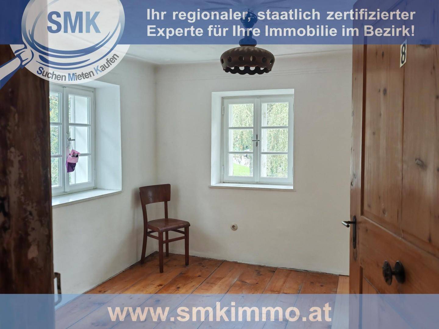 Einfaches Schlafzimmer mit Holzboden, zwei Fenstern und einer Holztür, die ins Freie führt.