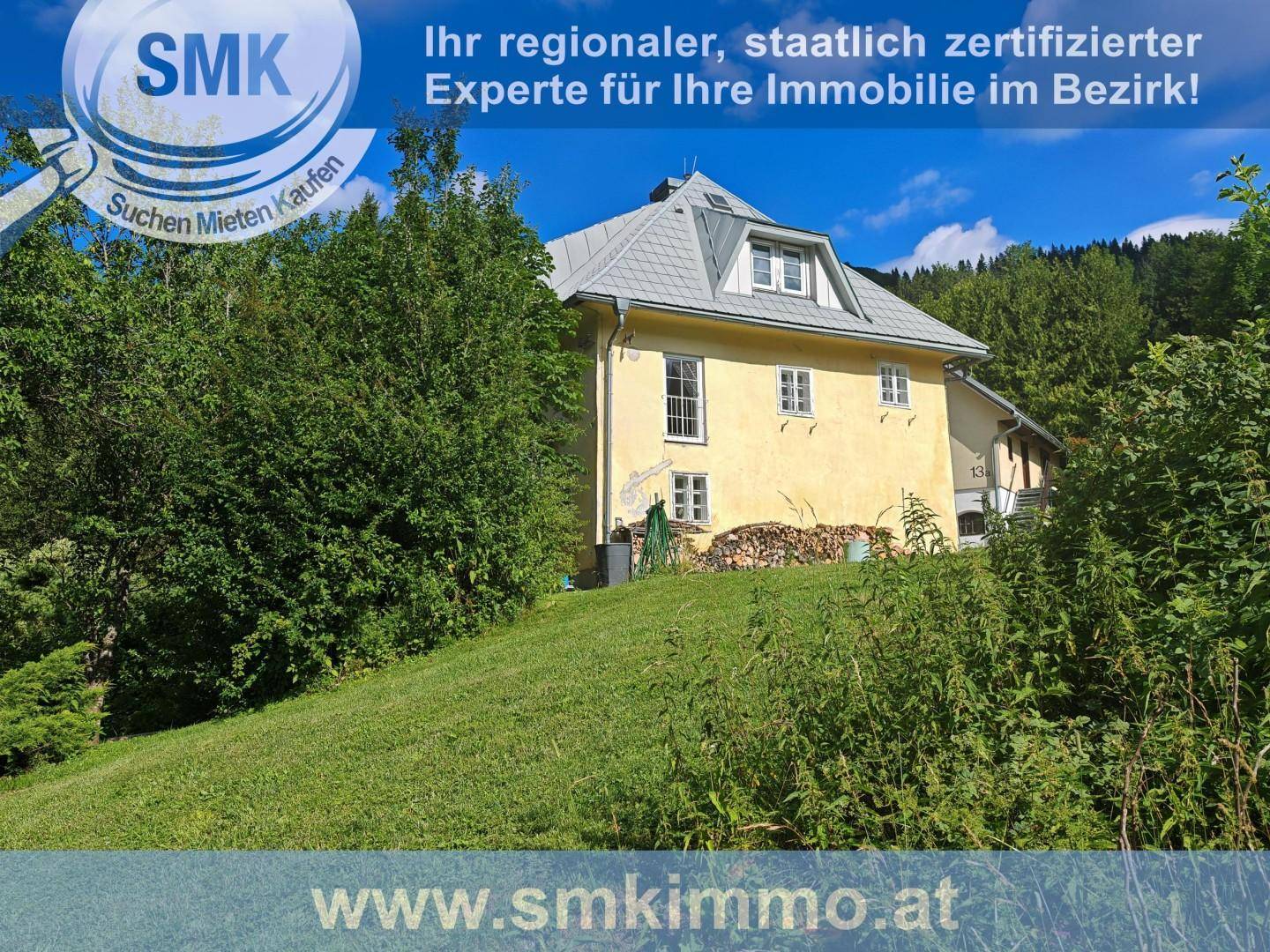 Gelb gestrichenes Haus mit grauen Dachziegeln, umgeben von üppiger grüner Vegetation und Hügeln.
