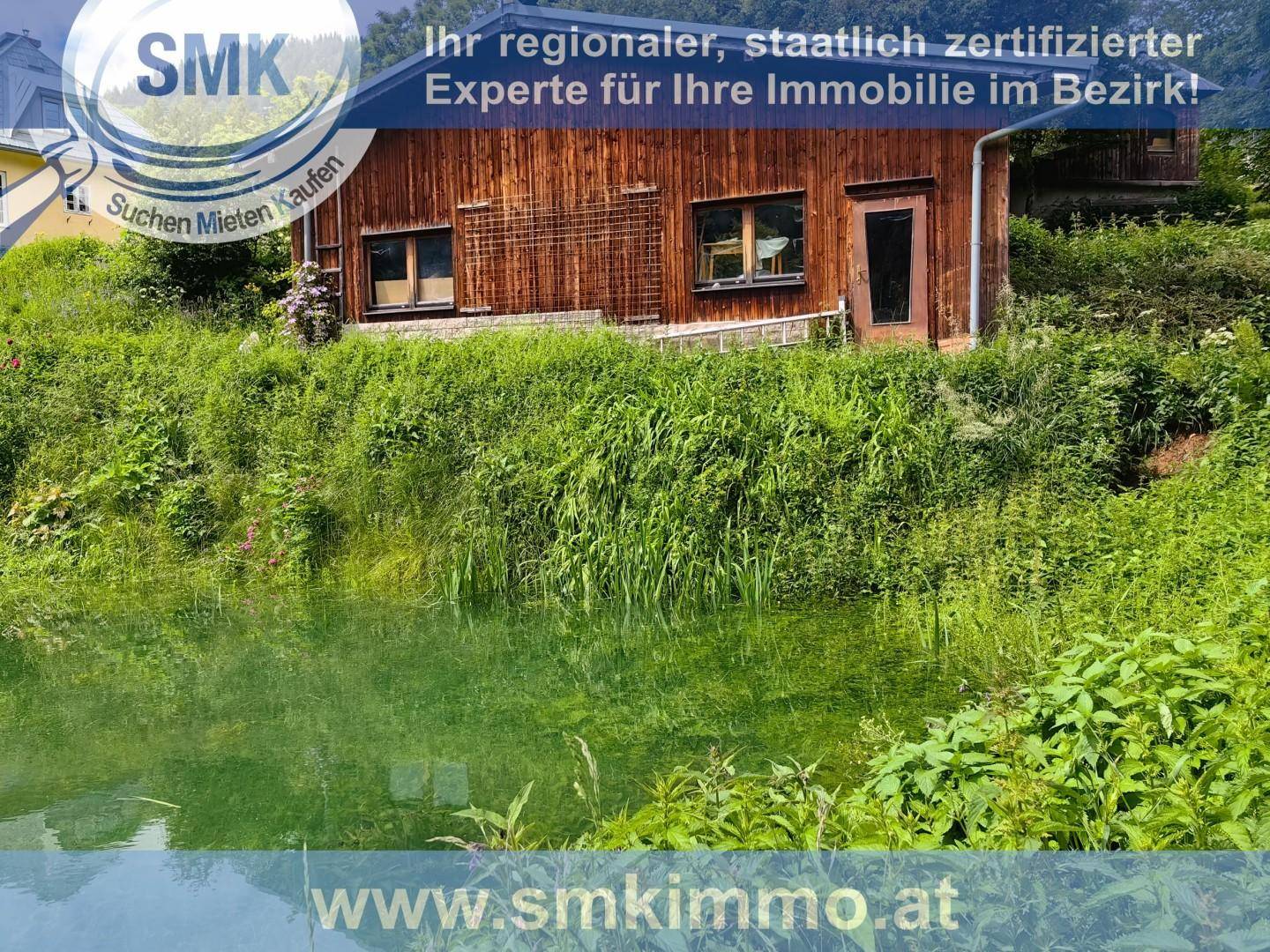 Natürlicher Teich im Vordergrund mit einem rustikalen Holzhaus im Hintergrund, umgeben von Vegetation.