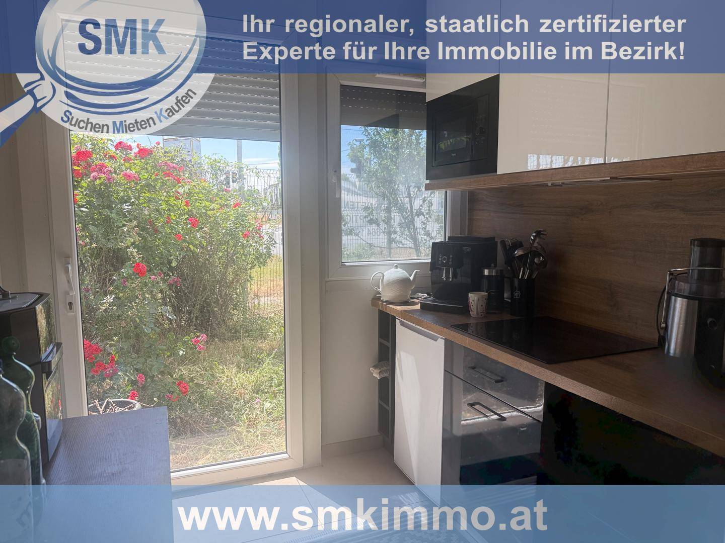 Kleine Küchenzeile mit Kaffeemaschine, Induktionskochfeld, Backofen und Blick auf Rosen durch das Fenster.