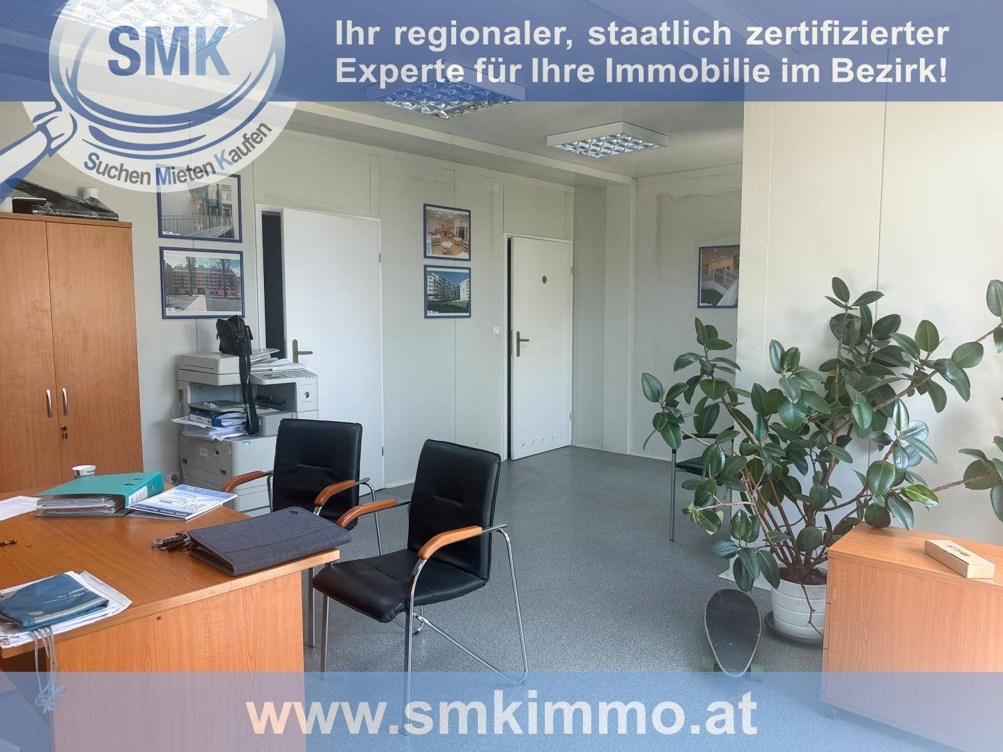 Büro mit Schreibtisch, Bürostühlen, Drucker und einer großen Zimmerpflanze, zwei Türen im Hintergrund.