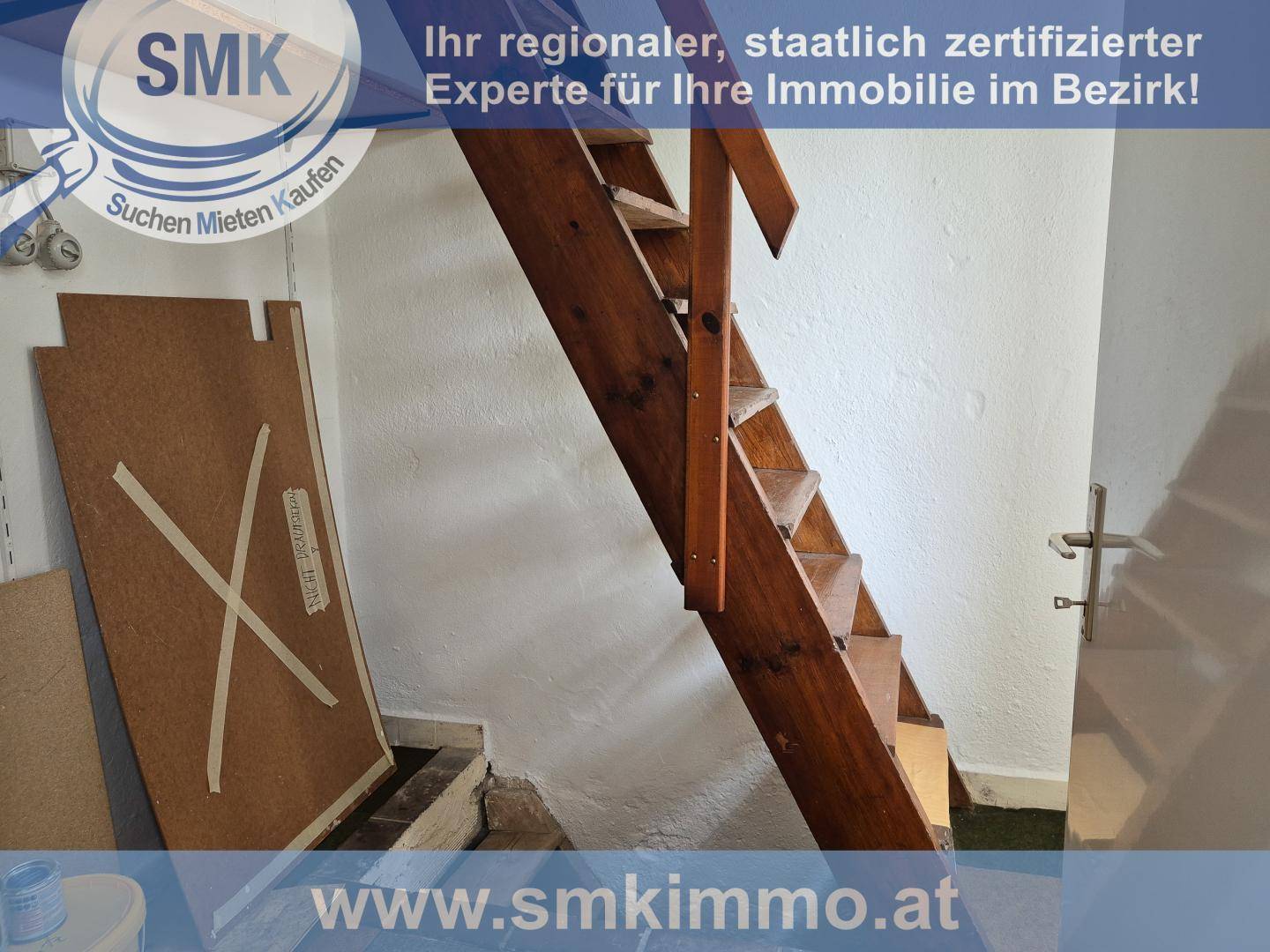 Holztreppe führt in ein oberes Stockwerk, umgeben von einfachen Wänden.