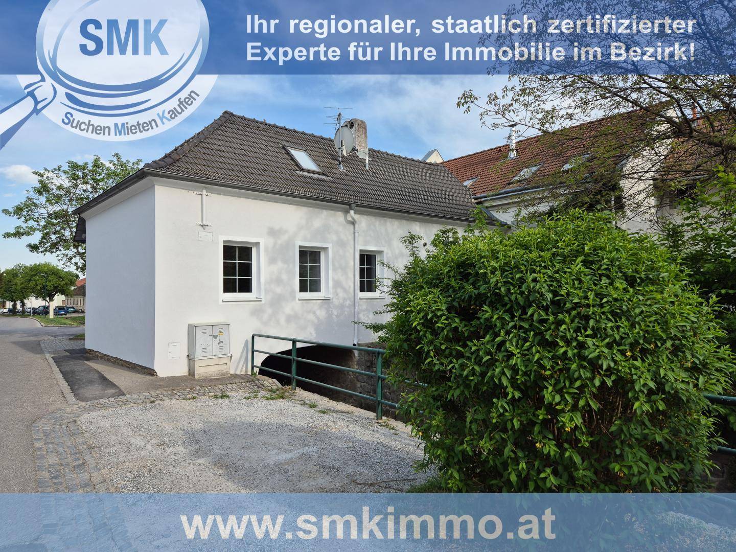 Seitenansicht des Hauses mit weißer Fassade, Satteldach und kleiner Zufahrt.