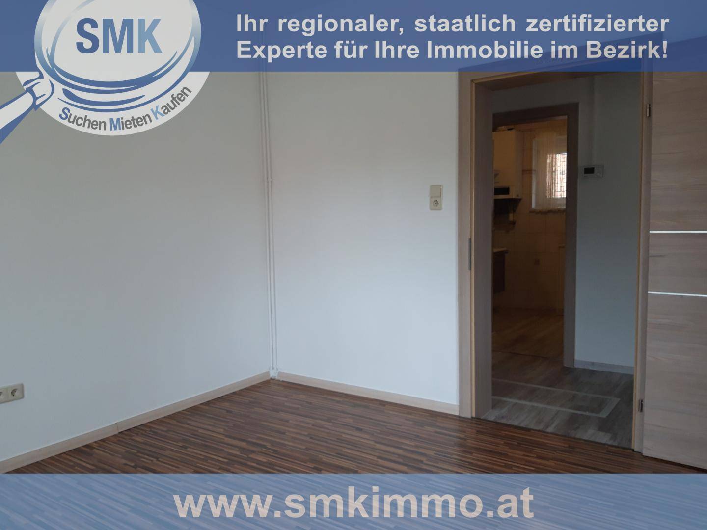 Leeres Zimmer mit Laminatboden, weißen Wänden und einem Türrahmen zu einem weiteren Raum.