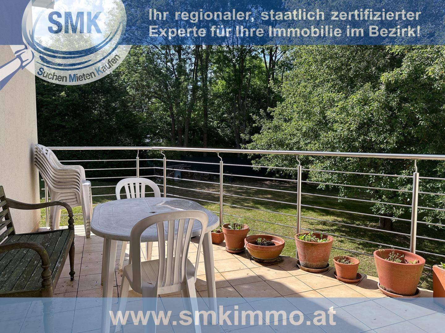 Balkon mit Gartenmöbeln und Topfpflanzen, umgeben von grüner Natur.