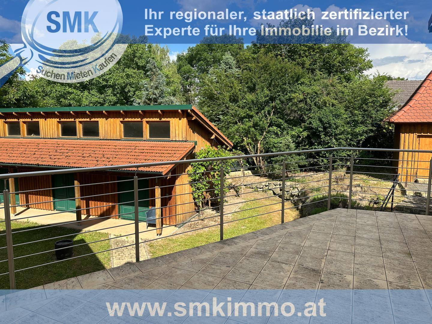 Terrasse mit Metallgeländer und Blick auf den Garten und ein Holzgebäude.