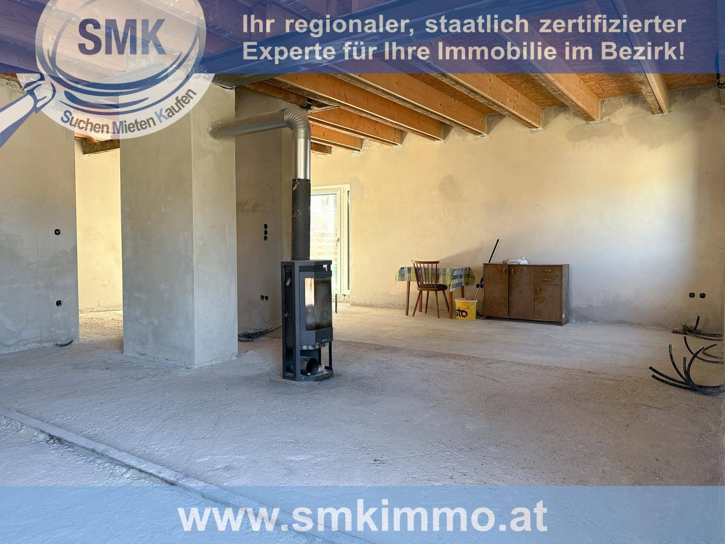 Rohbau eines Wohnraums mit sichtbaren Holzbalken und modernem Holzofen.