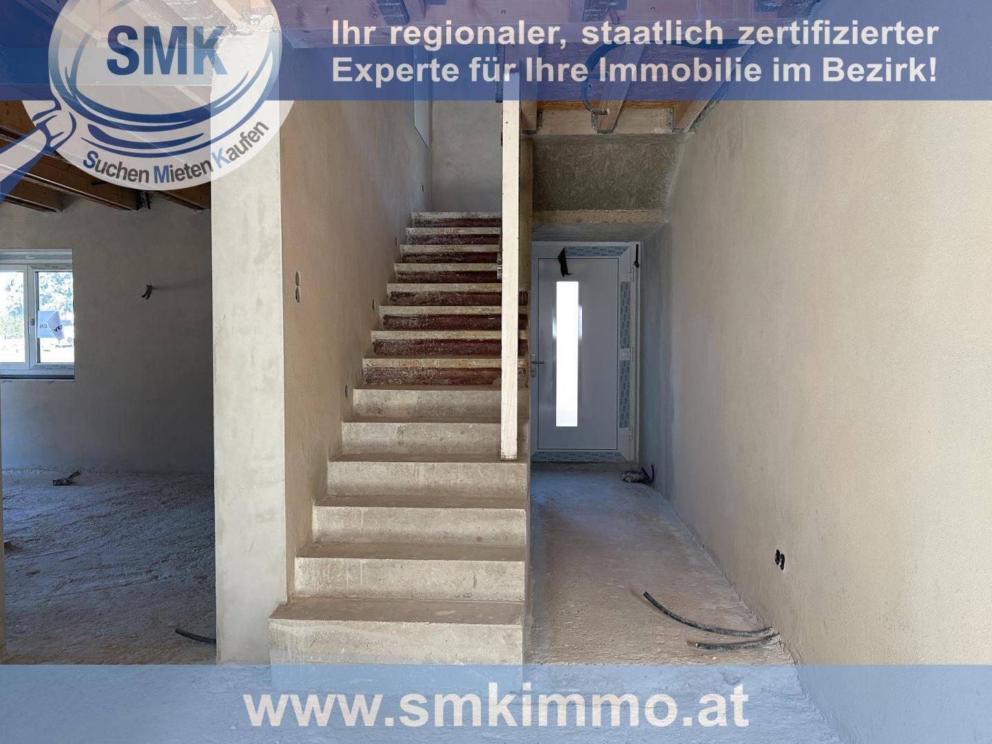Unfertiges Treppenhaus mit Betontreppe und Eingangstür in einem Rohbau.