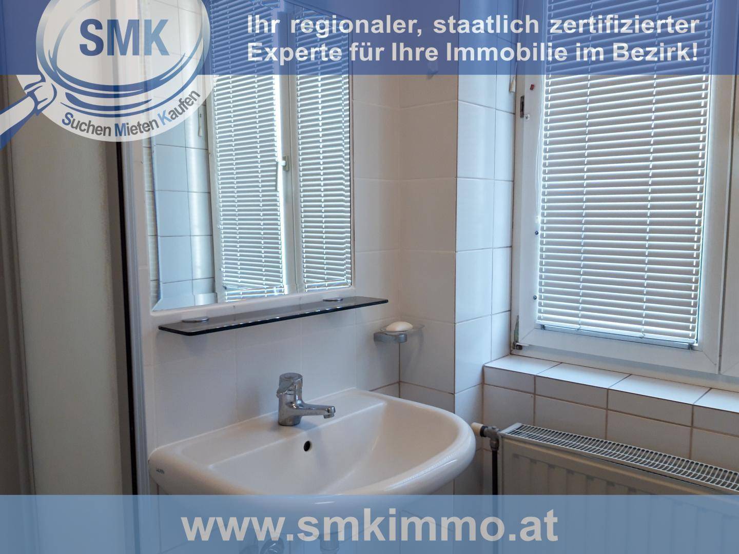 Badezimmer mit Waschbecken, Spiegel und weißen Fliesen an den Wänden, inklusive Fenster mit Jalousien.