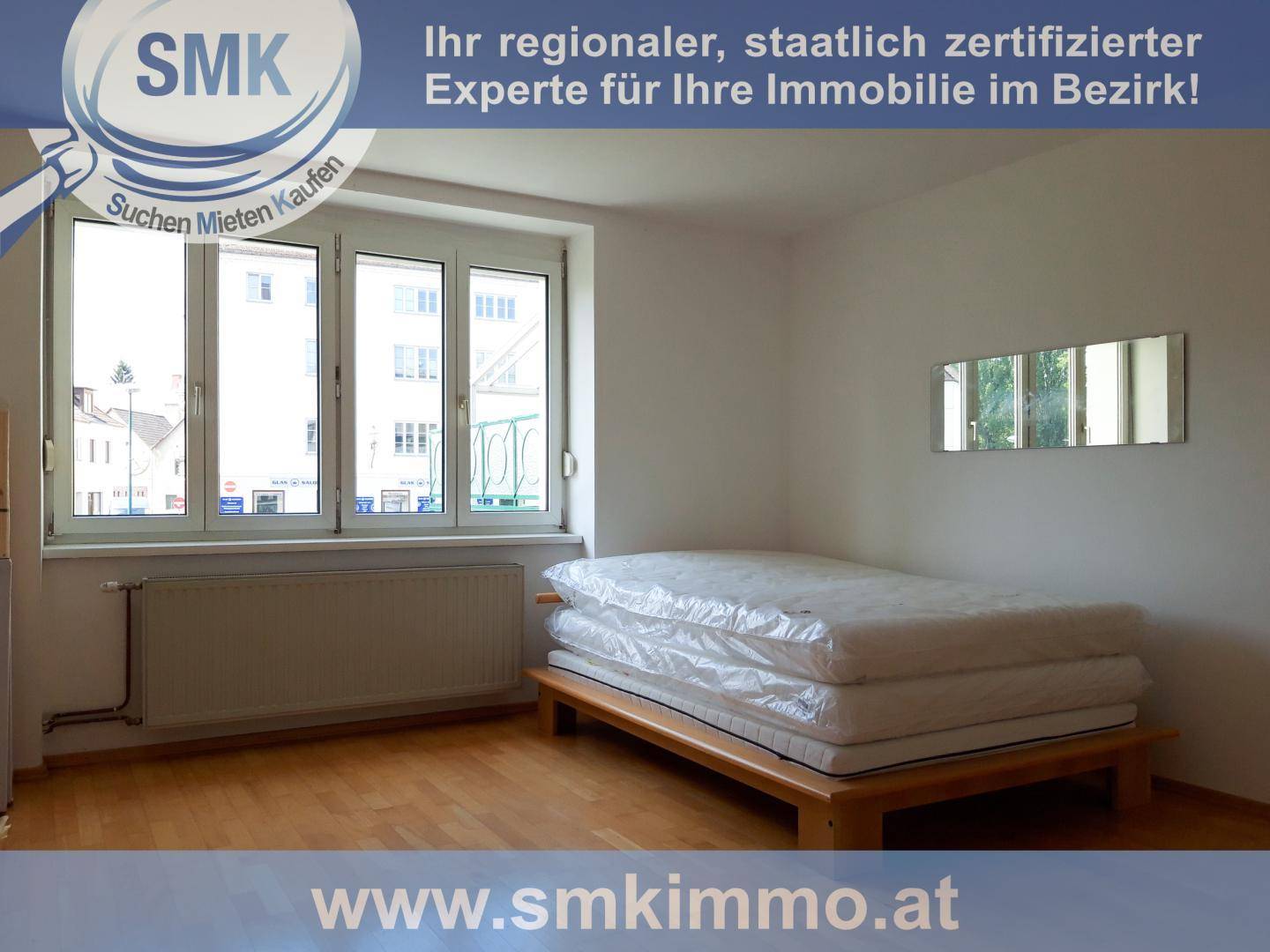 Schlafzimmer mit einfachem Holzbettgestell, Holzboden und großen Fenstern für eine helle Atmosphäre.