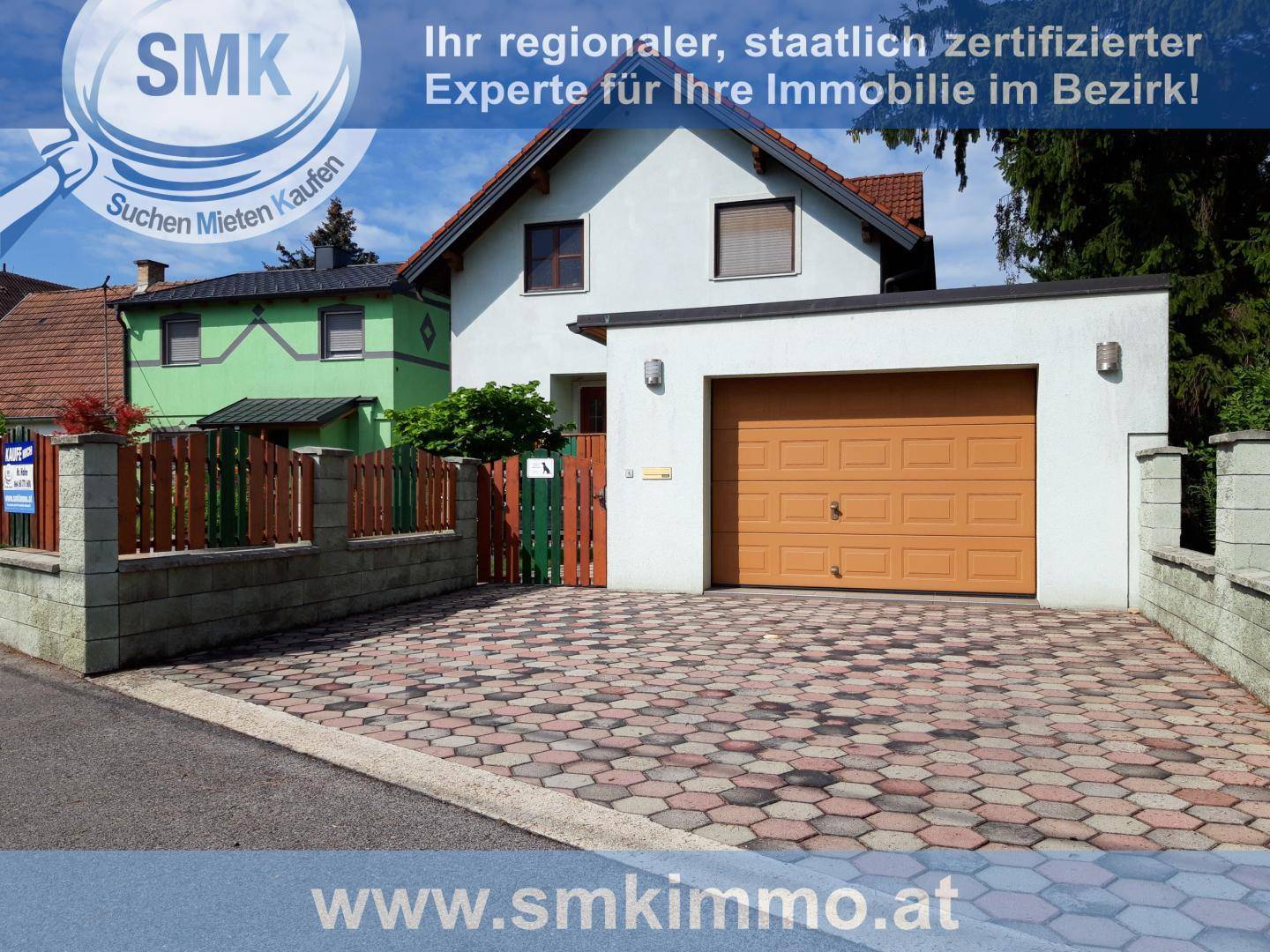 Weißes Einfamilienhaus mit integrierter Garage und gepflasterter Einfahrt für mehrere Fahrzeuge.
