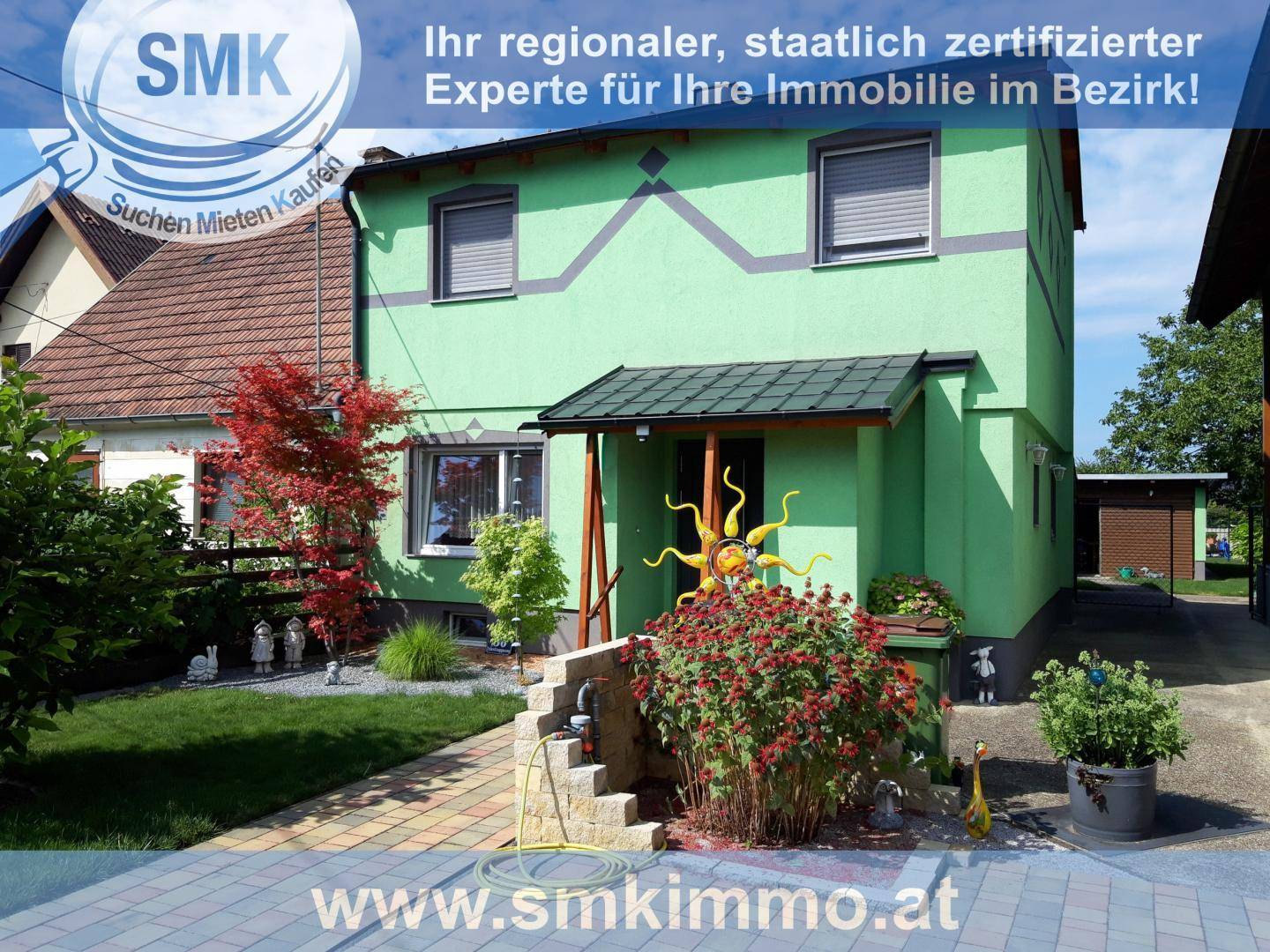 Grünes Einfamilienhaus mit Vordach, Vorgarten und dekorativen Elementen am Eingangsbereich.