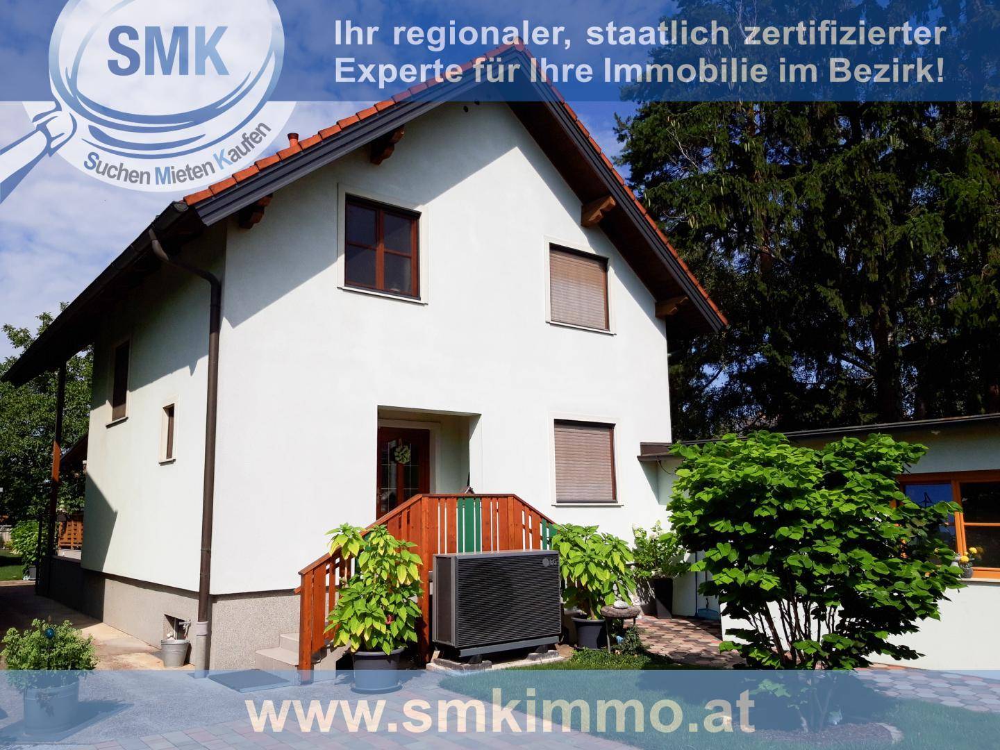 Weißes Einfamilienhaus mit Wärmepumpe, Holztreppe zum Eingang und umgebender Bepflanzung.