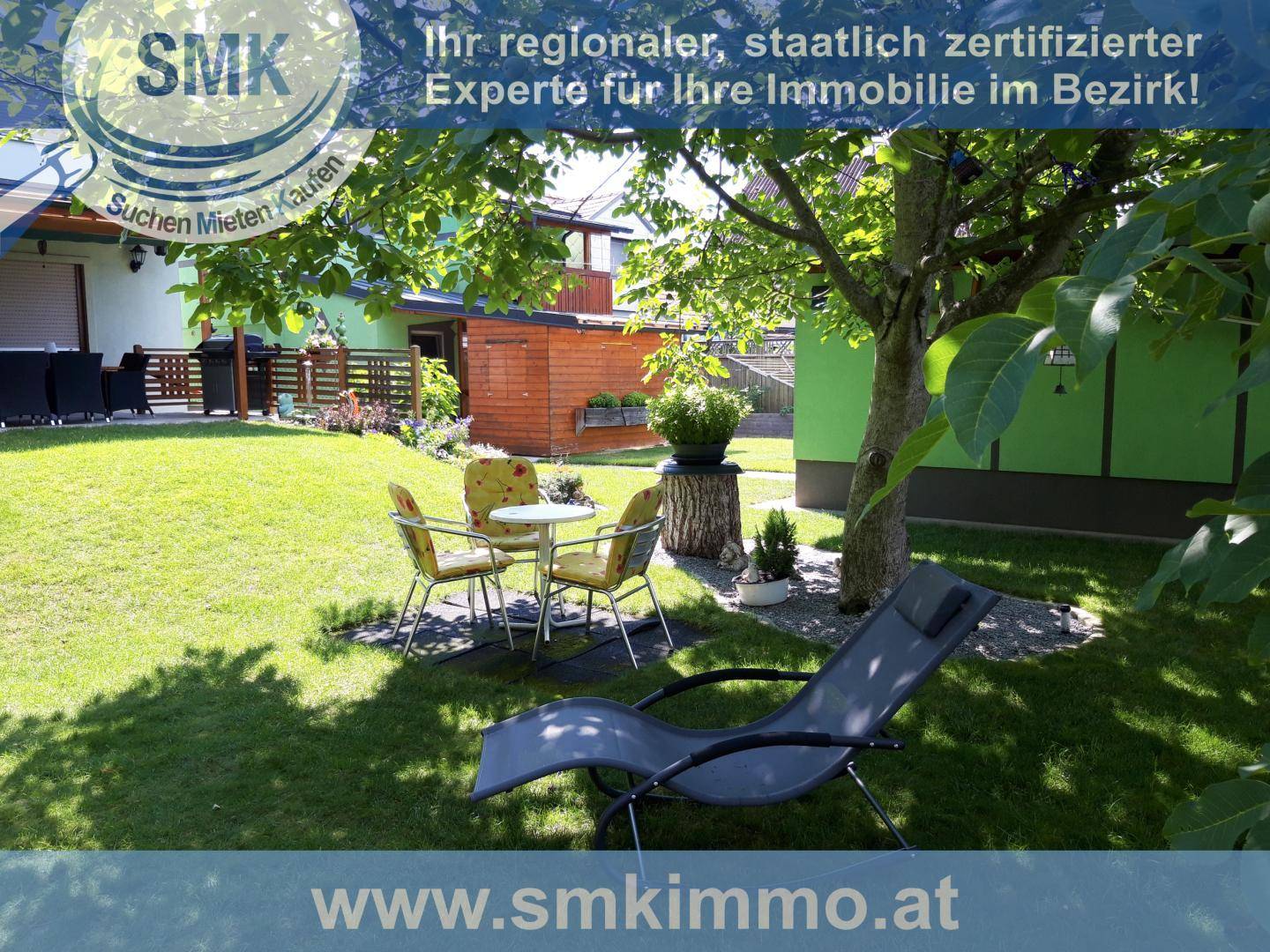 Gepflegter Garten mit Rasenfläche, schattenspendendem Baum und gemütlichen Sitzgelegenheiten im Freien.