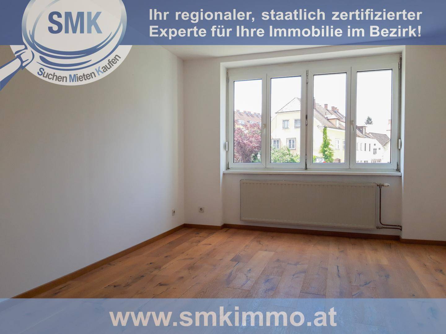 Leeres Zimmer mit Holzboden und großen Fenstern, die viel Tageslicht hereinlassen und einen Stadtblick bieten.