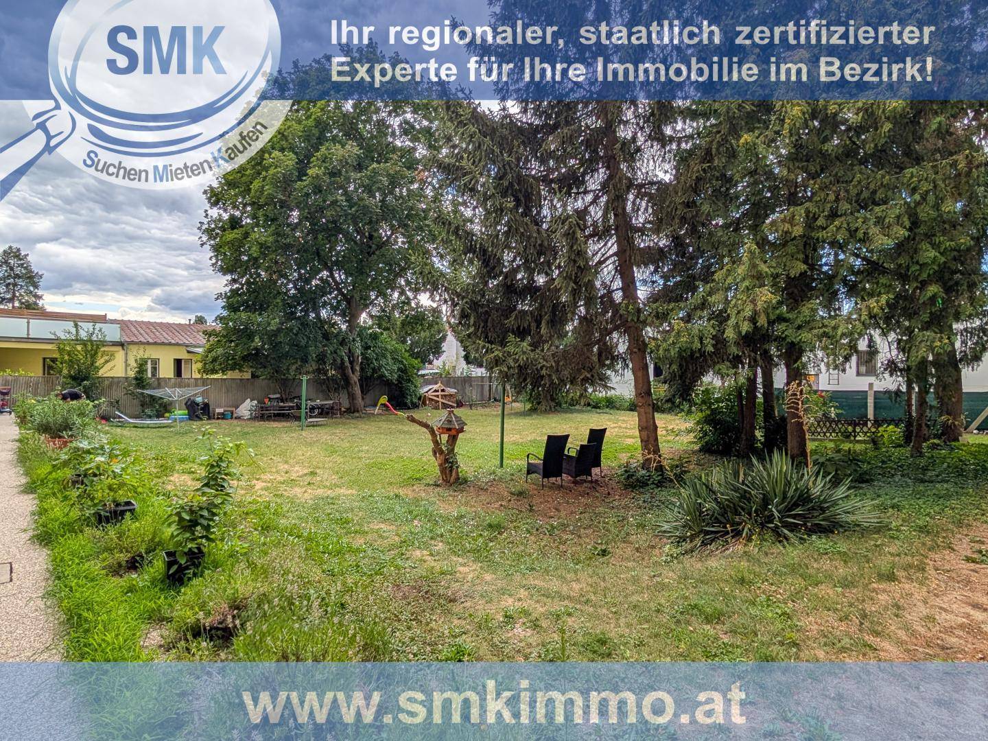 Großer Gartenbereich mit Rasenfläche, alten Bäumen und einer kleinen Sitzecke im Freien.