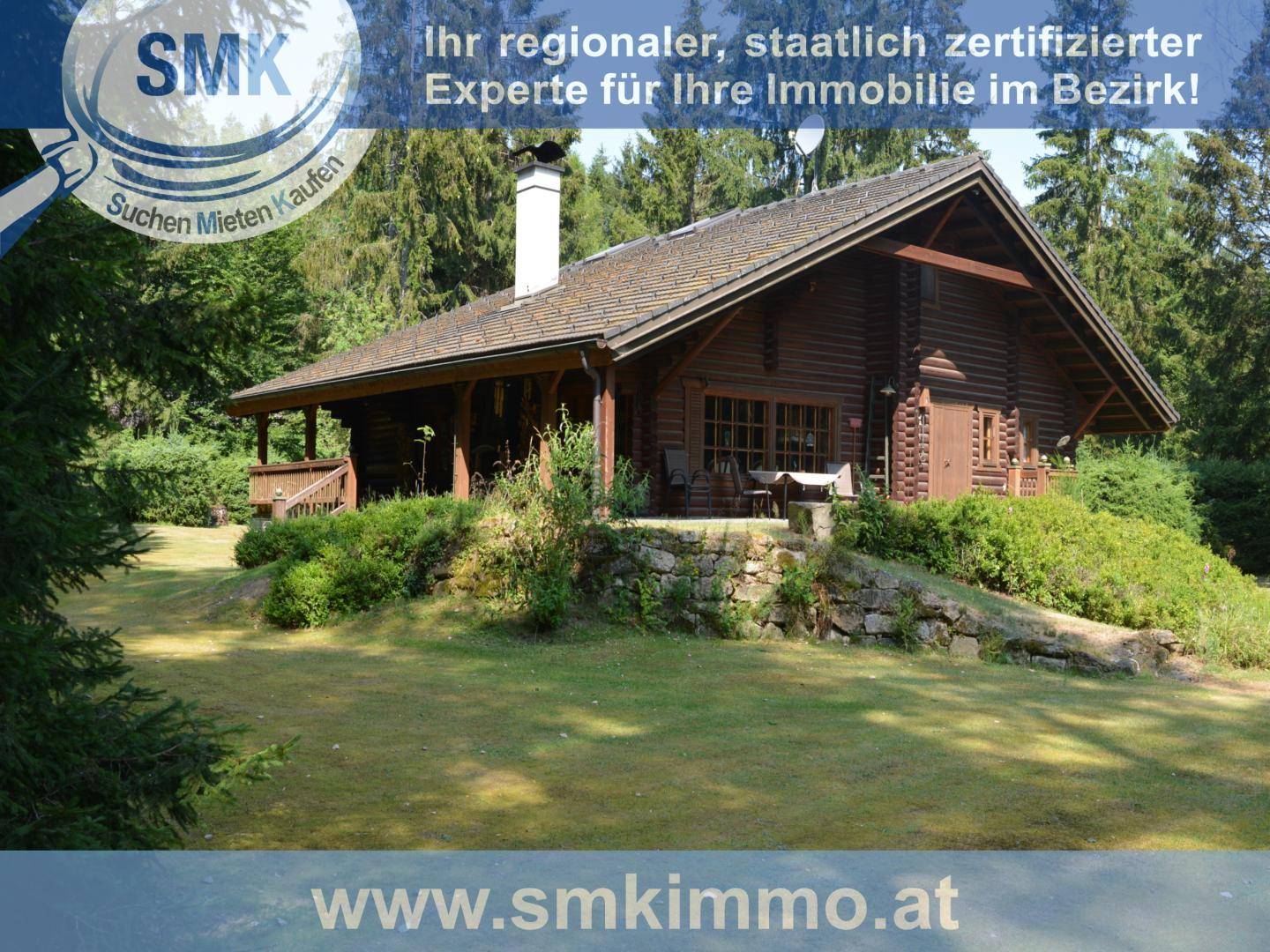 Seitenansicht der Blockhütte mit überdachtem Bereich und kleiner Terrasse im Grünen.