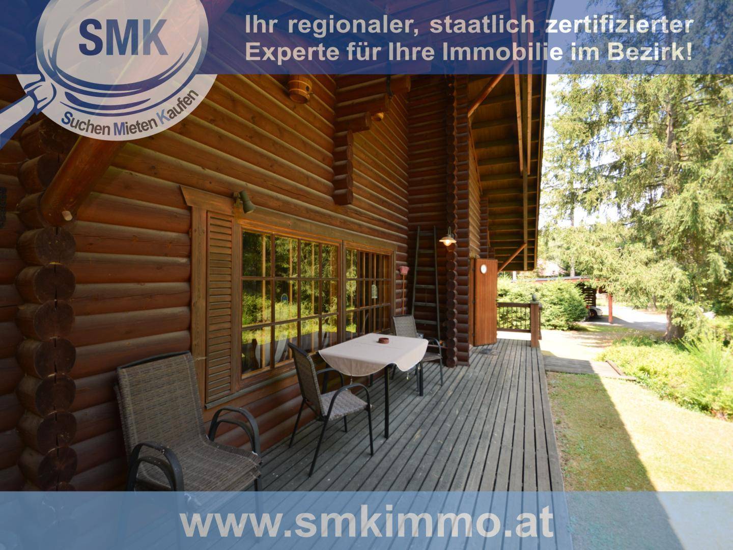 Gemütliche Holzterrasse an der Blockhütte mit kleinem Tisch und Stühlen im Freien.