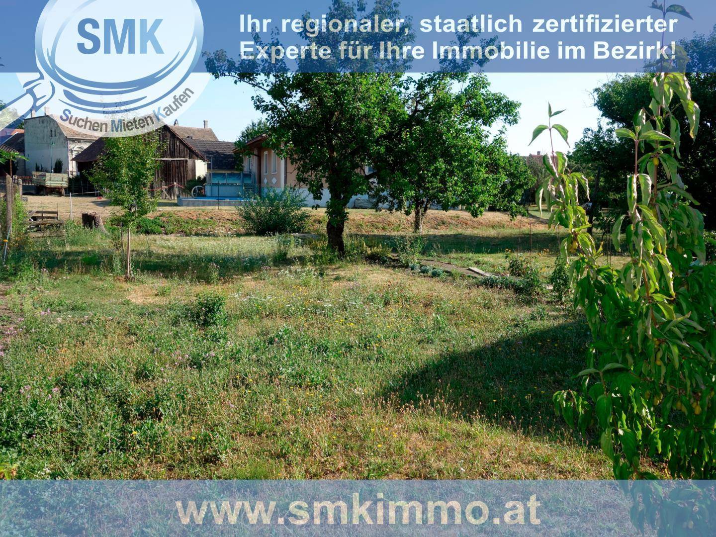 Weitläufiges Gartengrundstück mit Bäumen, Sträuchern und ländlicher Bebauung im Hintergrund.