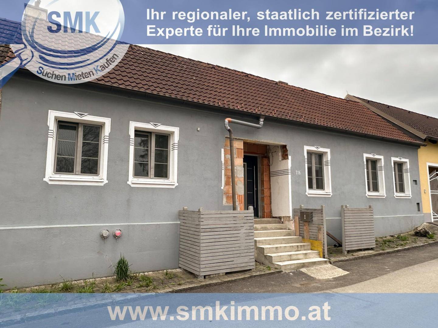 Fassade eines Hauses mit grauer Putzfassade und Eingangsbereich in Renovierung.