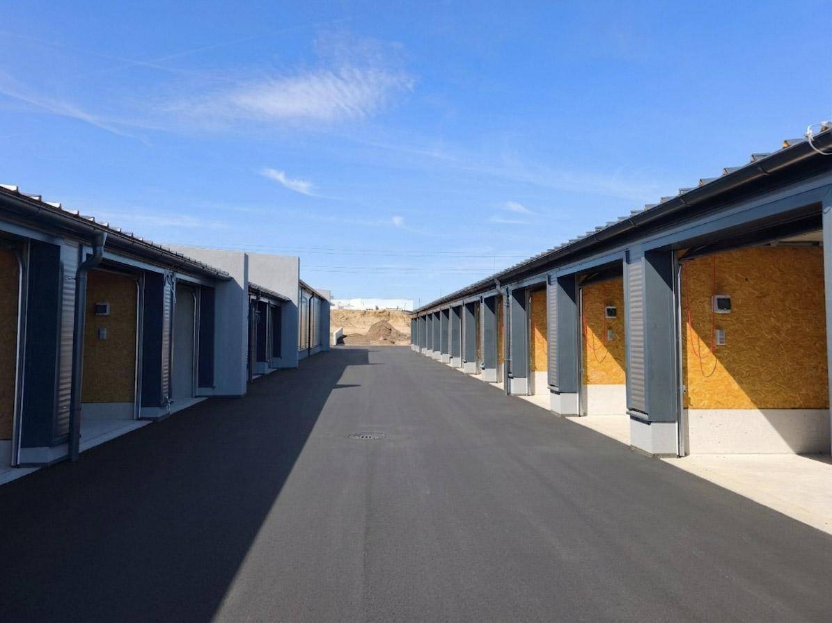Reihe von Lagerhallen mit geöffneten Rolltoren, die den Blick auf die holzverkleideten Innenräume freigeben.