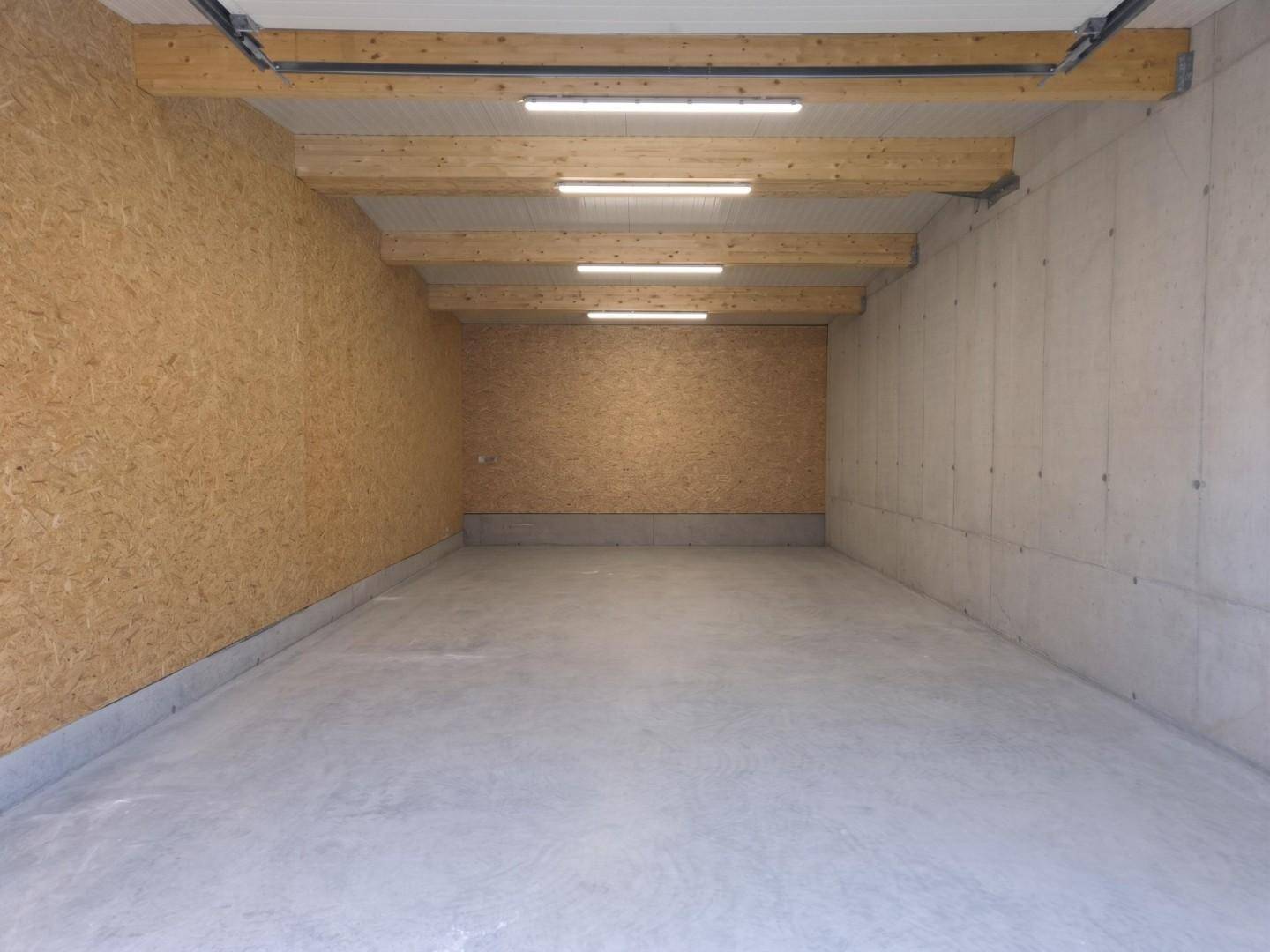 Helle Lagerhalle mit OSB-Platten, Betonwänden und sichtbaren Holzträgern mit Beleuchtung.