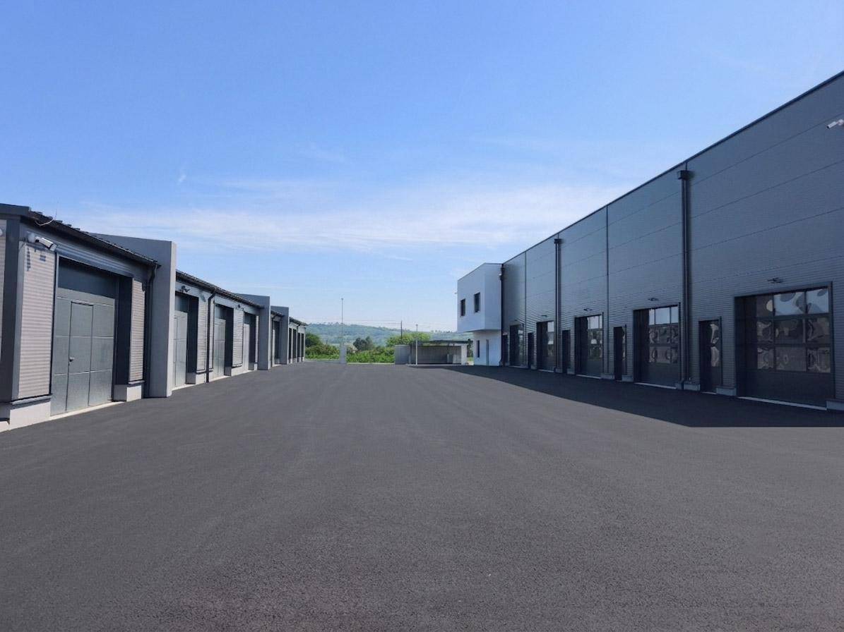 Ansicht eines modernen Gewerbeparks mit Lagerhallen und einem Bürogebäude, umgeben von asphaltierten Flächen.