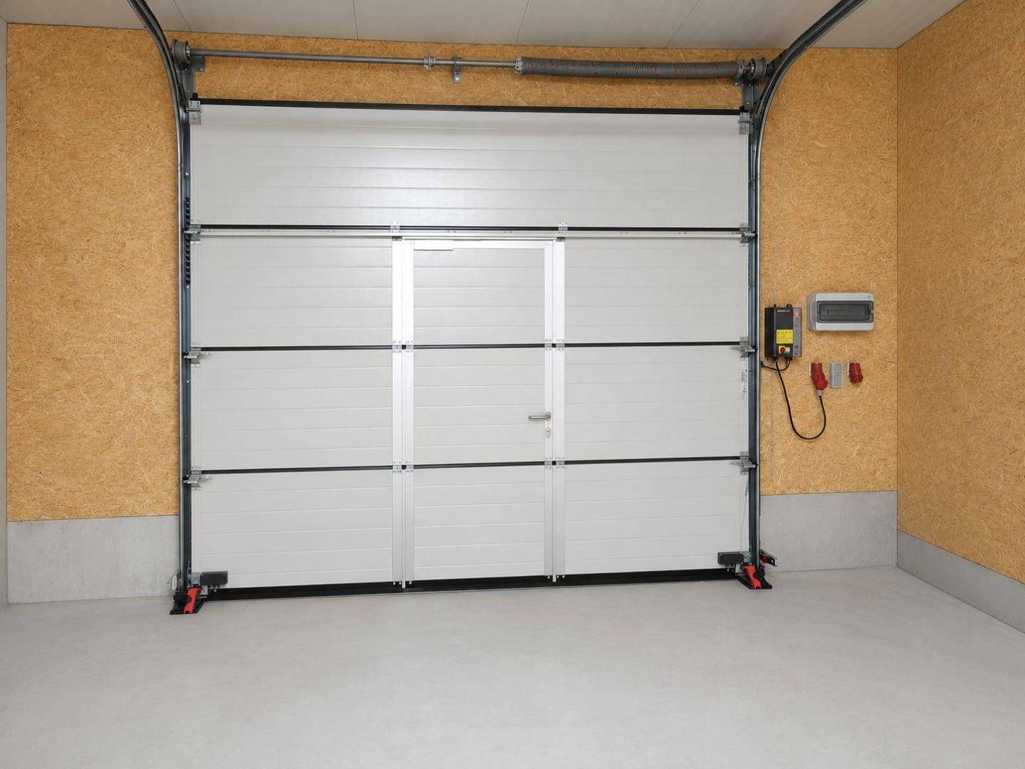 Innenansicht eines Garagentors mit integrierter Tür und elektrischem Anschluss in einer Lagerhalle.