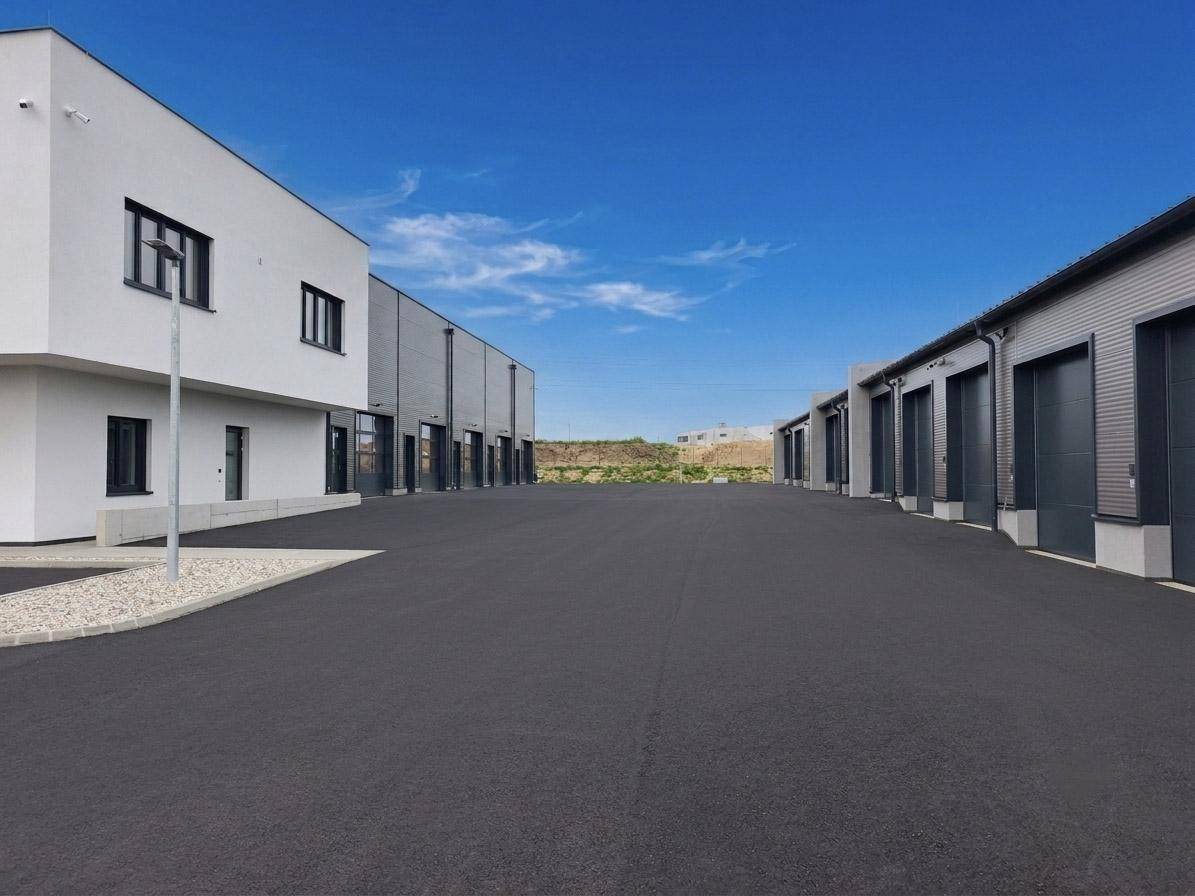 Weitläufiger Außenbereich mit modernen Lagerhallen und einem weißen Bürogebäude unter blauem Himmel.