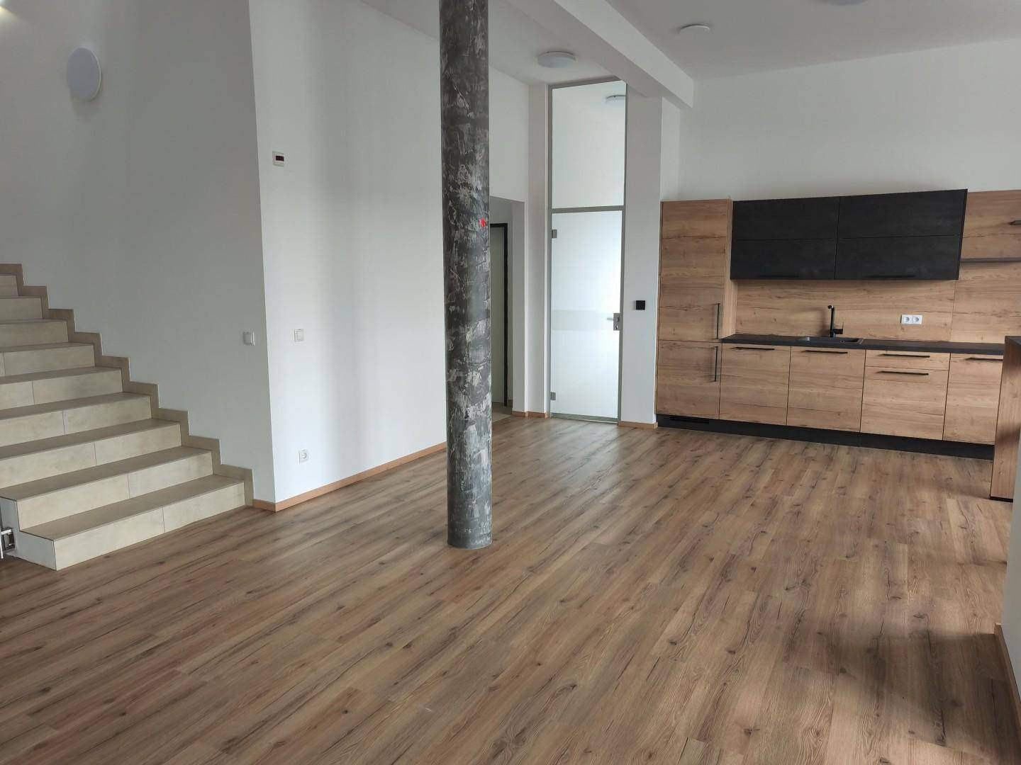 Großer offener Raum mit Laminatboden, Treppe, Küchenzeile und einem markanten Betonpfeiler.