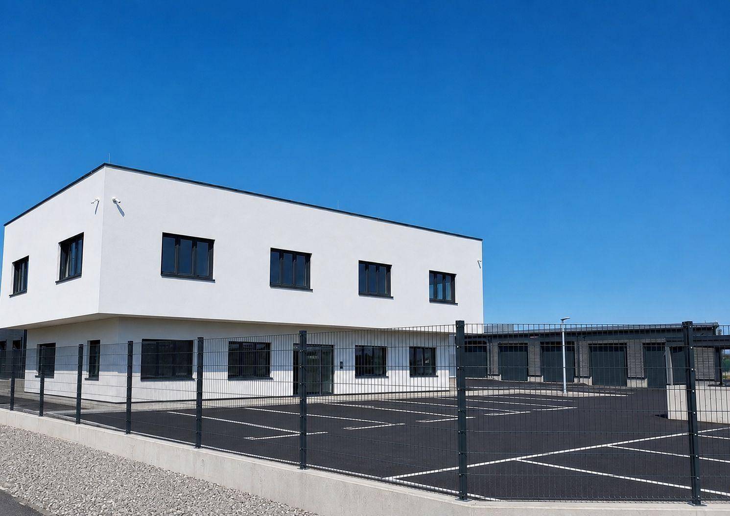 Ansicht des modernen Bürogebäudes mit Parkplatz und Zaun unter klarem blauem Himmel.
