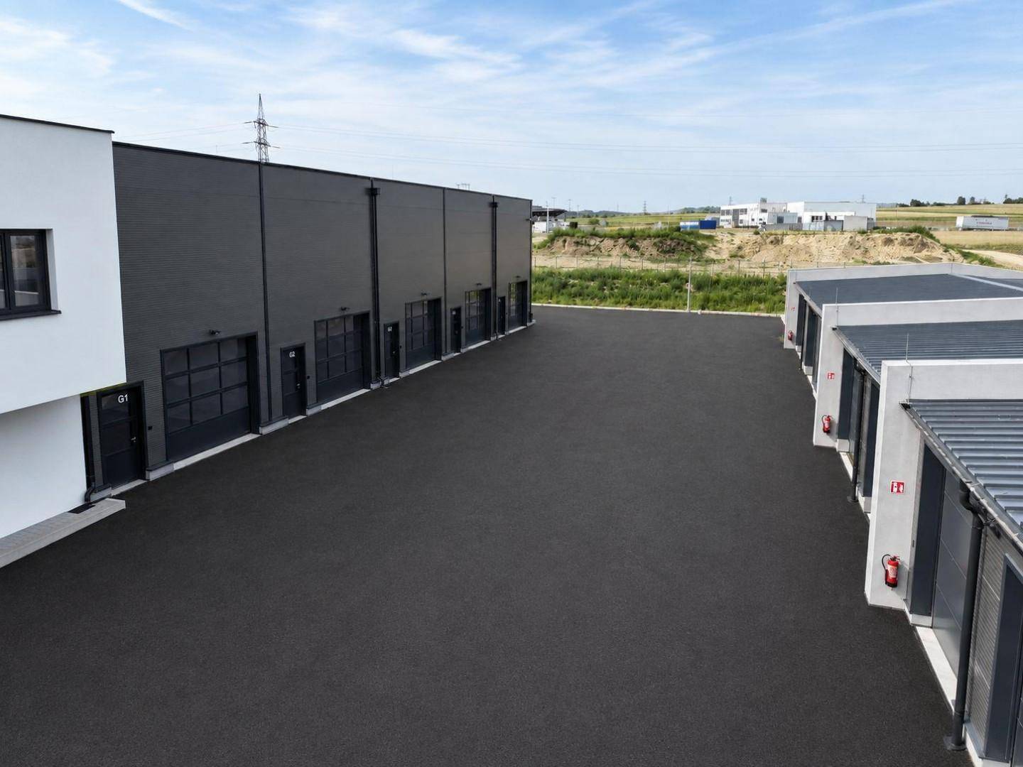 Rückansicht des Gebäudekomplexes mit mehreren Garagen und einer großen asphaltierten Fläche.