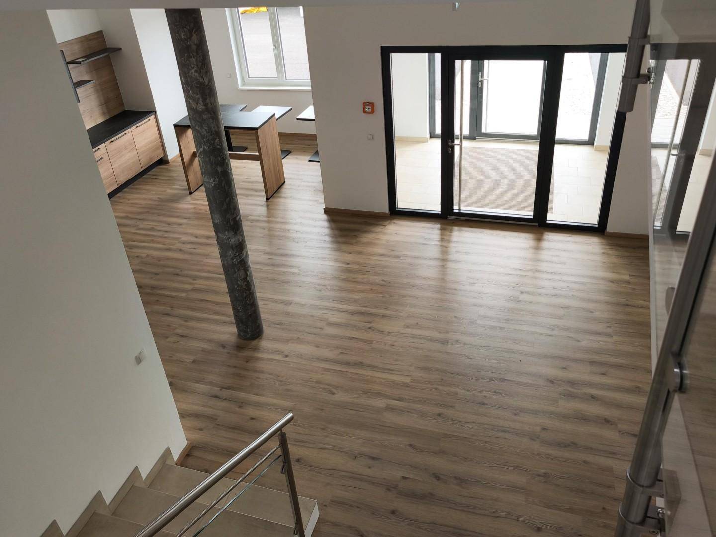 Blick von oben auf den offenen Bürobereich mit Laminatboden und großen Glastüren zum Außenbereich.