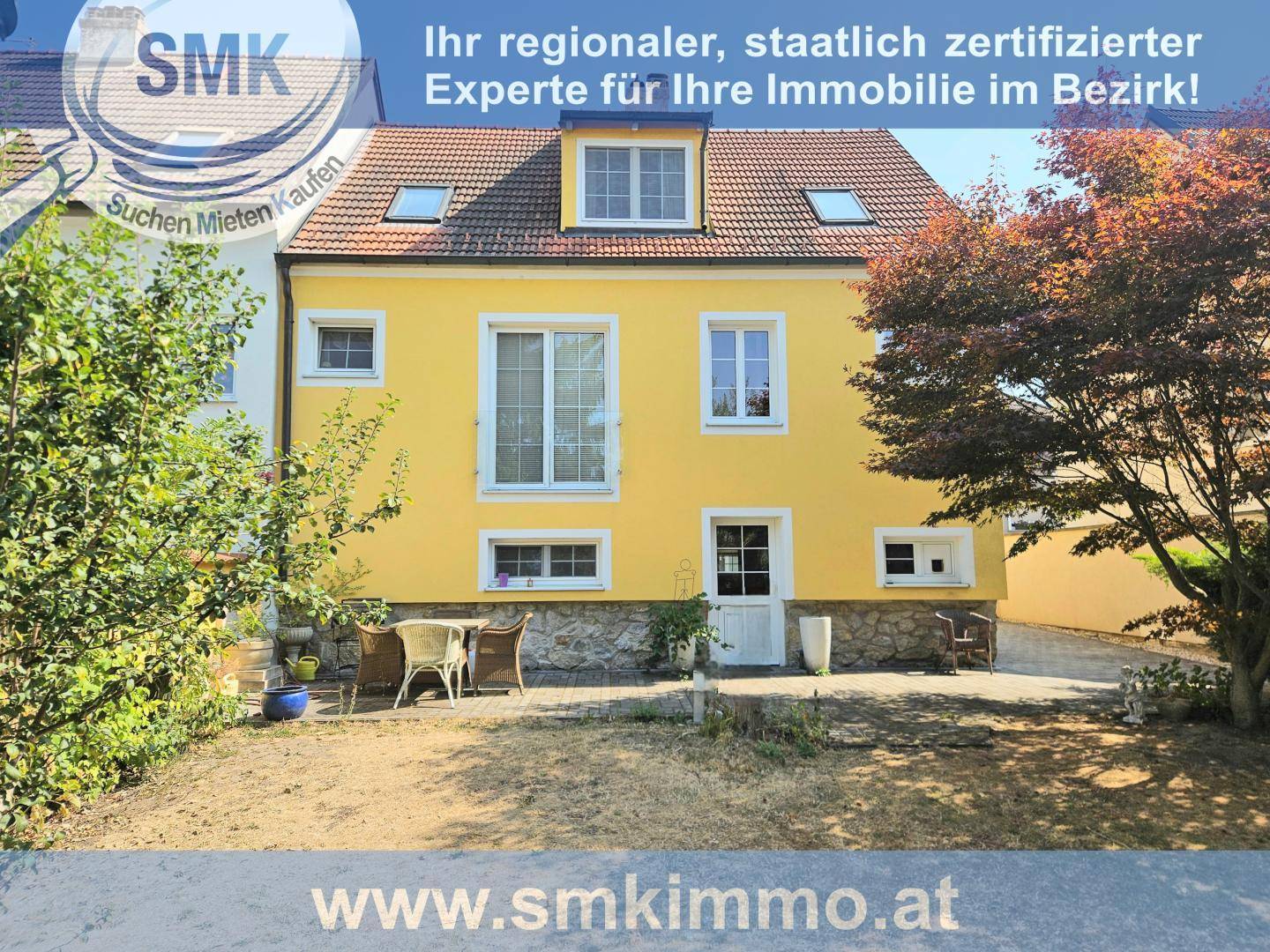Rückansicht des gelben Hauses mit kleinem Gartenbereich und Sitzgelegenheiten im Freien.