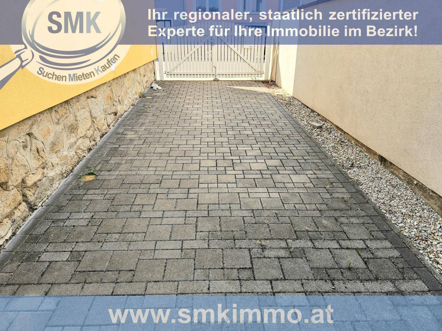Gepflasterte Einfahrt oder Parkplatz vor dem Haus mit einem Tor.